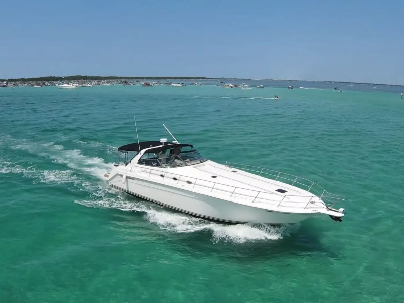 White yacht cruising on turquoise water near a crowded beach.