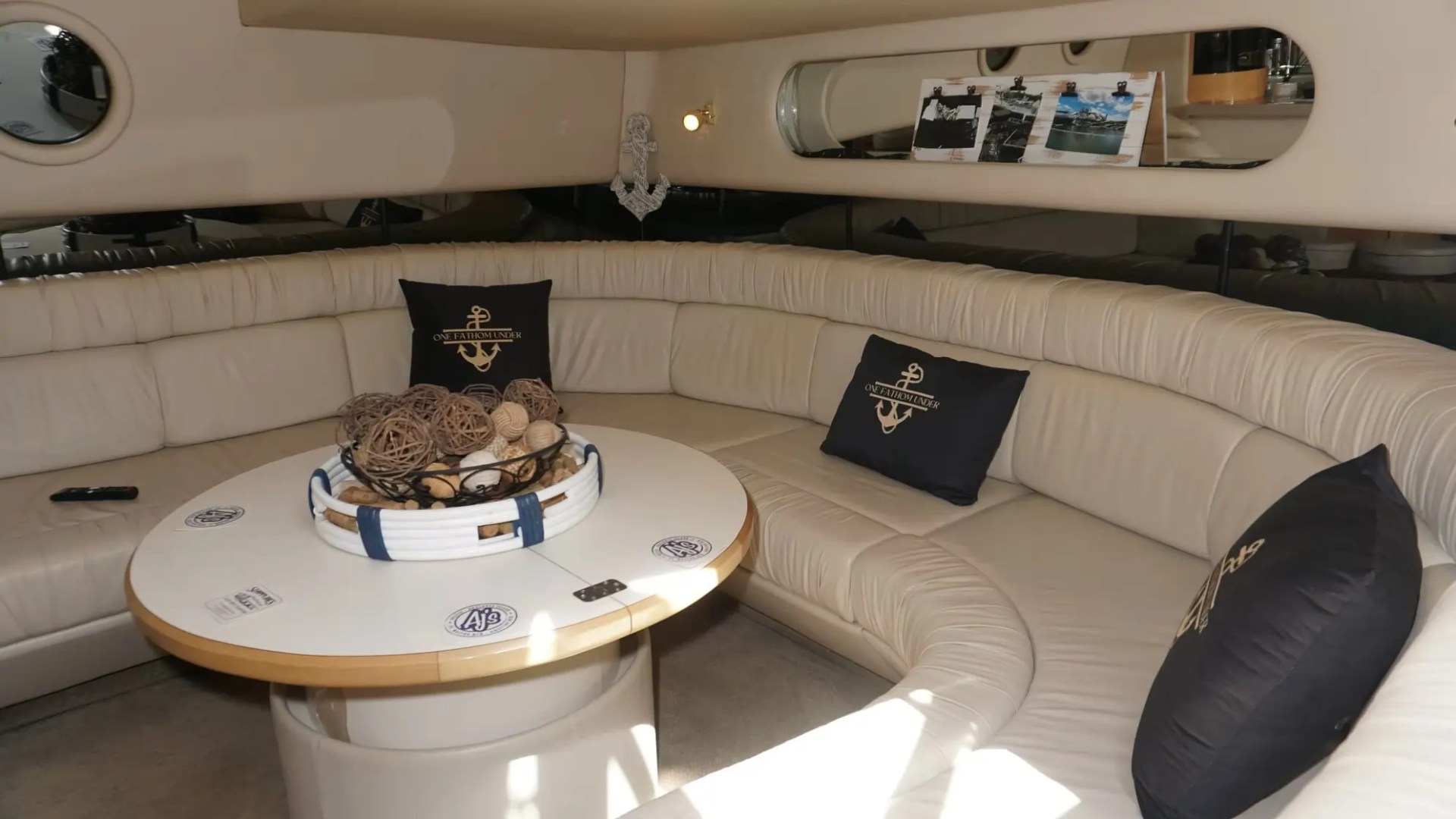 Luxurious yacht interior with curved beige seating, decorative pillows, and a round table centerpiece.