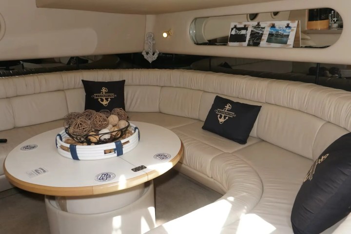 Luxurious yacht interior with curved beige seating, decorative pillows, and a round table centerpiece.