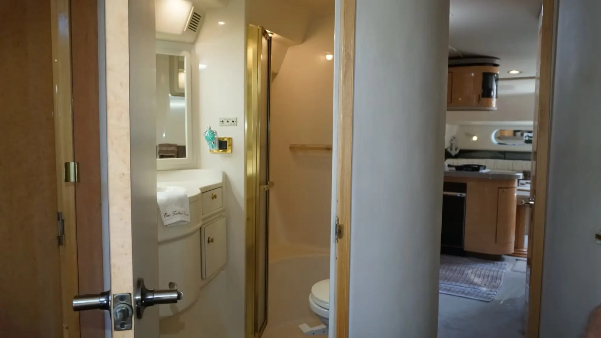 Interior of a boat showing a bathroom and a small kitchen area visible through open doors.