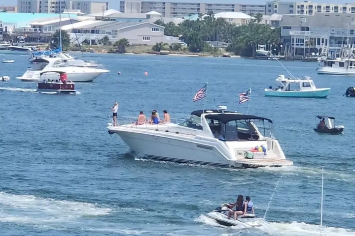 Boats of various sizes on a busy waterway near a town with buildings in the background.