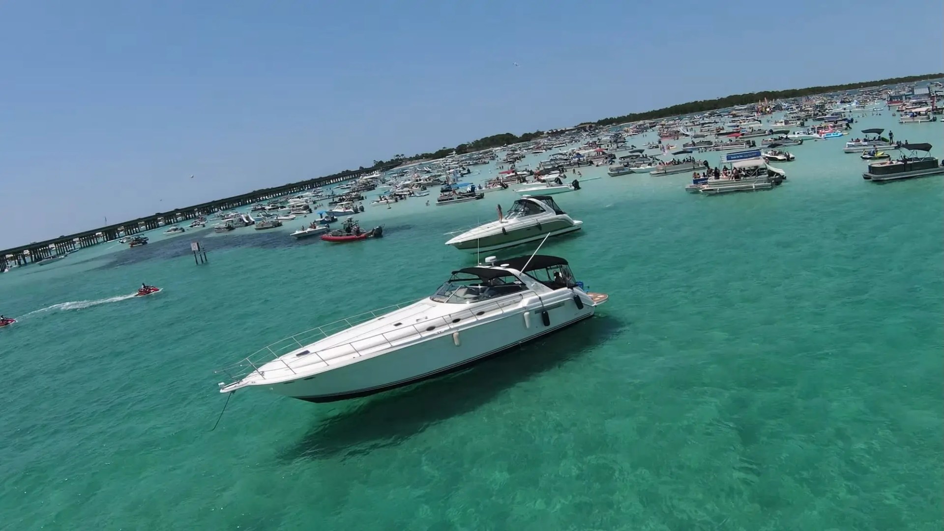 Boats and jet skis on turquoise water with a crowded beach in the background.