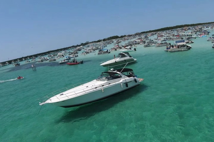 Boats and jet skis on turquoise water with a crowded beach in the background.