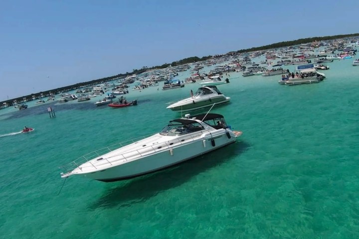 Boats anchored in clear turquoise water on a sunny day with people enjoying the scene.