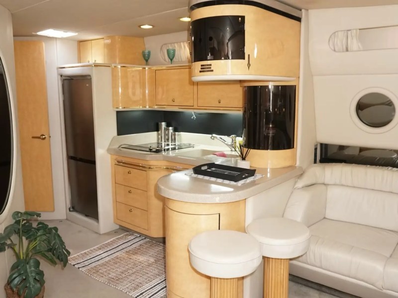 Luxury yacht interior with kitchen, curved sofa, stools, and round windows.