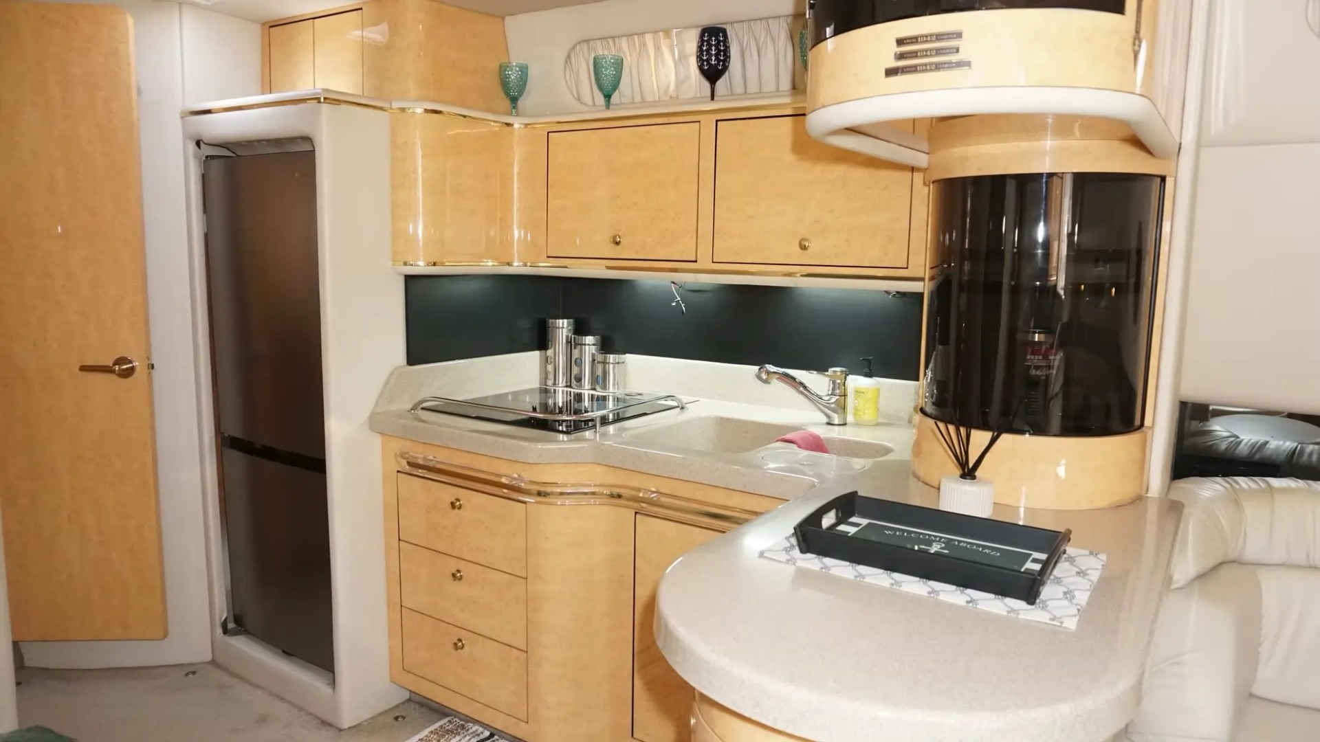 Compact kitchen with wood cabinets, fridge, sink, and counter in a light-toned, modern design.