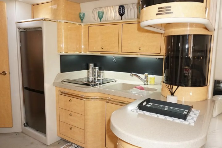 Compact kitchen with wood cabinets, fridge, sink, and counter in a light-toned, modern design.