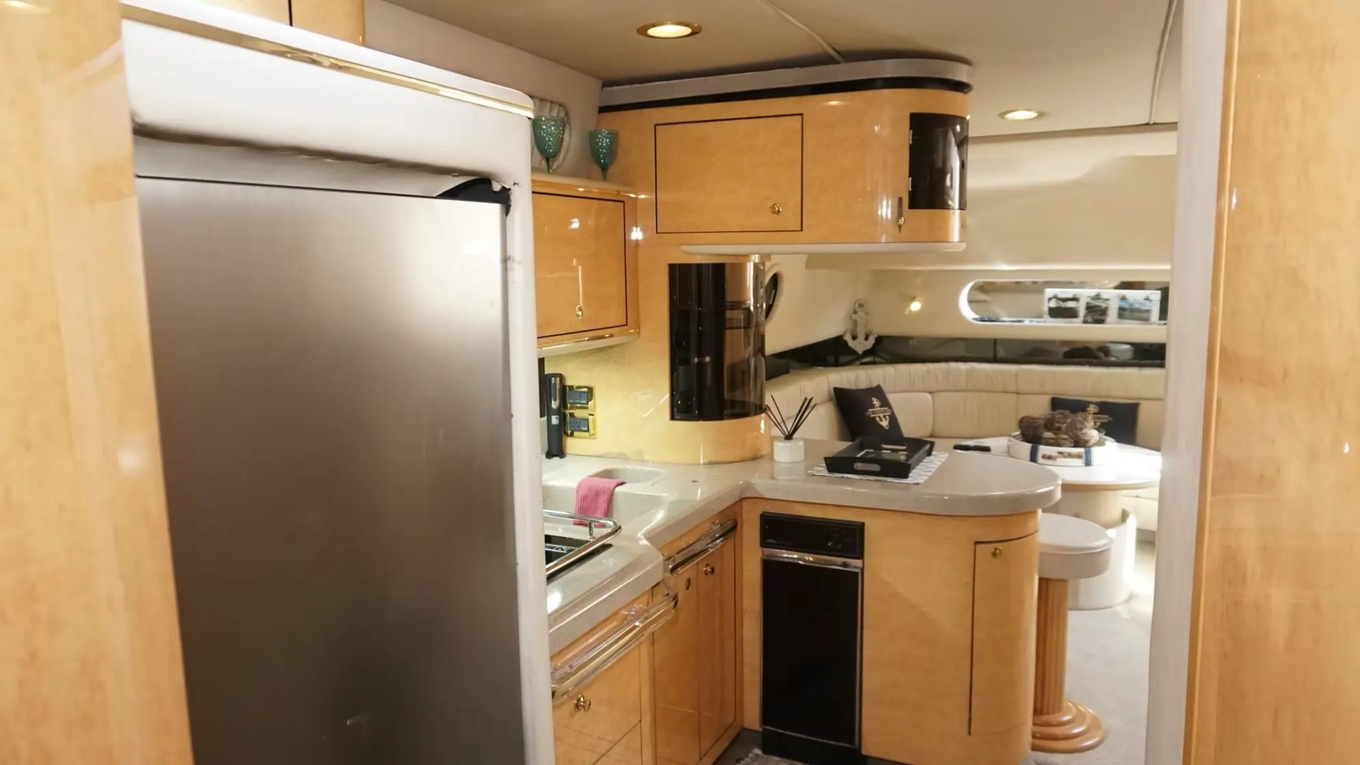 Modern yacht kitchen with wooden cabinets and lounge area in the background.