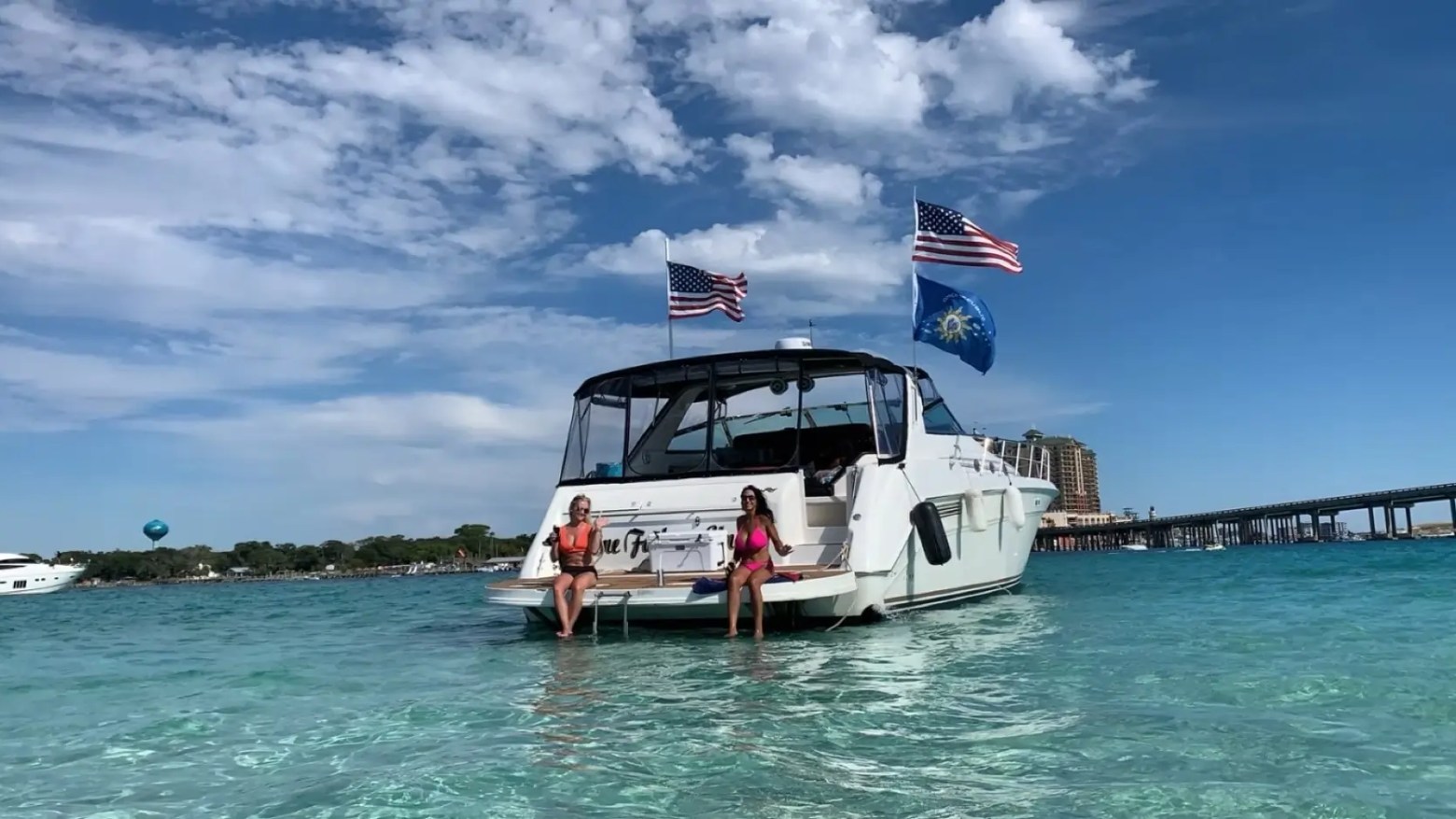 Two people sitting on a boat with USA flags, in clear water under a blue sky.