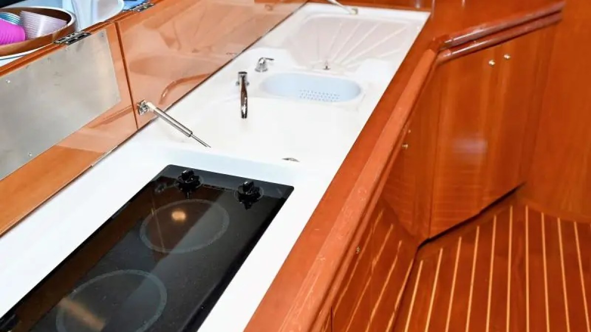 Boat kitchenette with stovetop, sink, and wooden cabinets.
