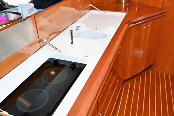 Boat kitchenette with stovetop, sink, and wooden cabinets.