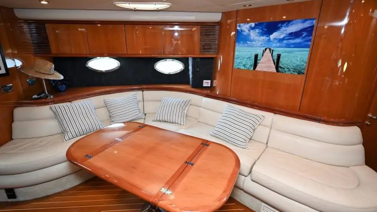 Luxurious yacht interior with beige sofa, wood table, and ocean photo on wall.