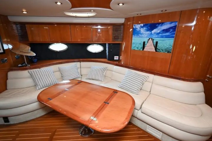 Luxurious yacht interior with beige sofa, wood table, and ocean photo on wall.