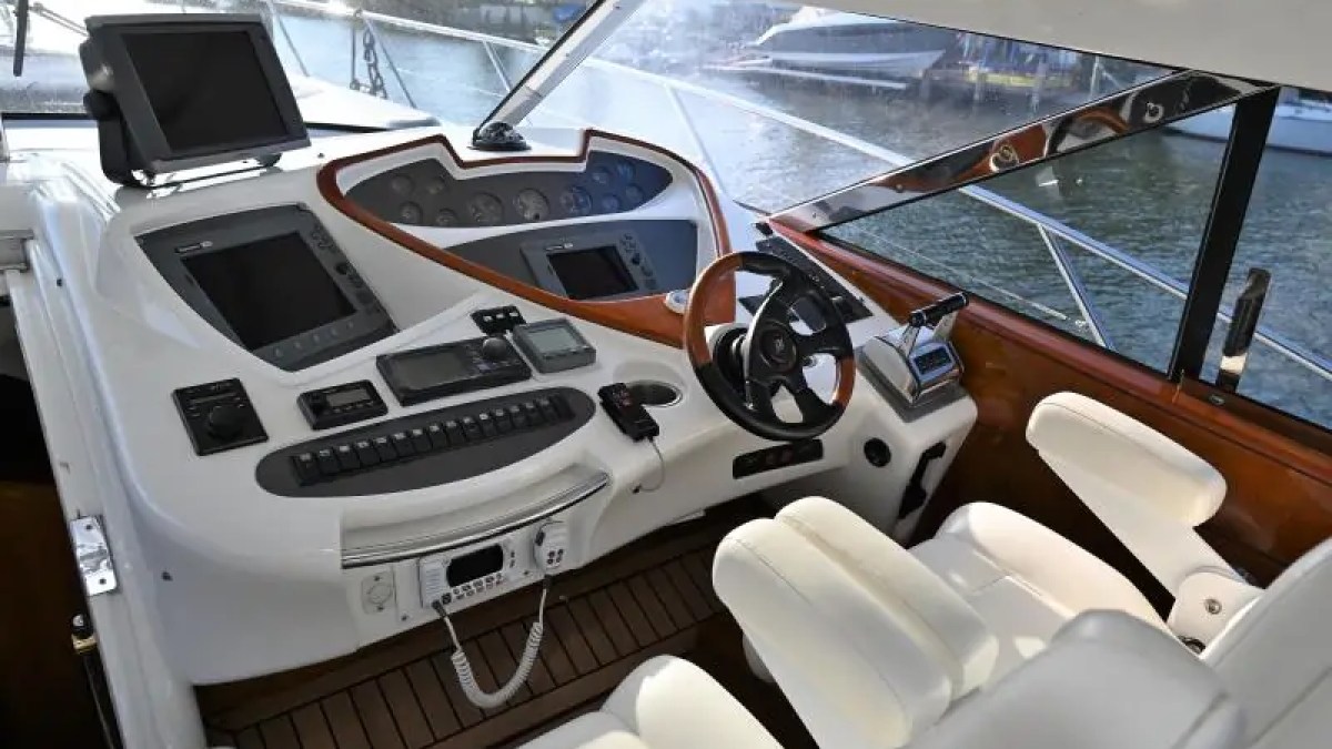 Interior of a boat cockpit with steering wheel, controls, and white seats.