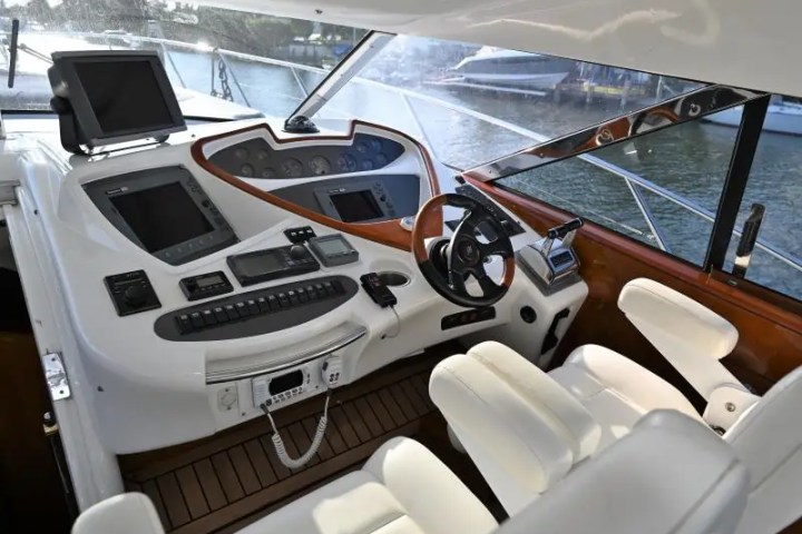 Interior of a boat cockpit with steering wheel, controls, and white seats.