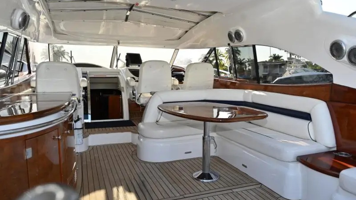 Interior of a luxury yacht with cushioned seating, wooden tables, and steering area.