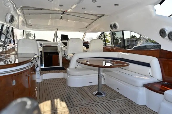 Interior of a luxury yacht with cushioned seating, wooden tables, and steering area.