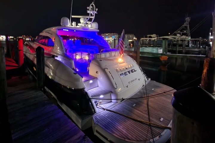 Luxury yacht docked at night, illuminated with blue and red lights, American flag visible.
