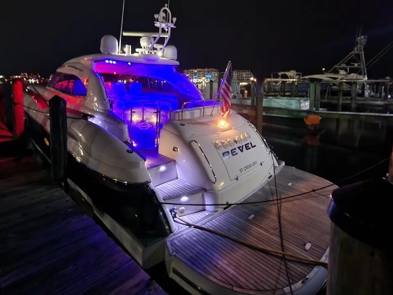 Luxury yacht docked at night, illuminated with blue and red lights, American flag visible.