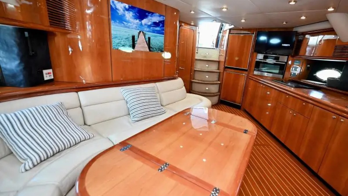 Luxurious yacht interior with wood paneling, beige sofa, striped pillows, and a scenic ocean photo on the wall.