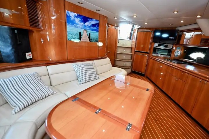 Luxurious yacht interior with wood paneling, beige sofa, striped pillows, and a scenic ocean photo on the wall.