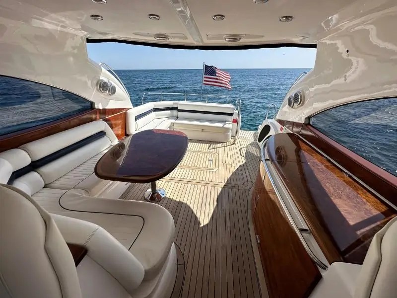 Luxury yacht deck with white seating, wooden table, and American flag, overlooking the sea.