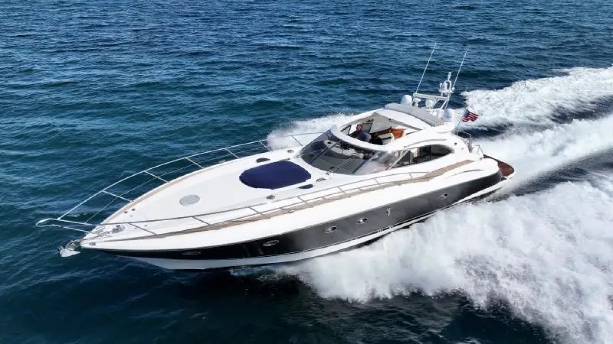 A sleek motor yacht cruising on the ocean with a city skyline in the background.