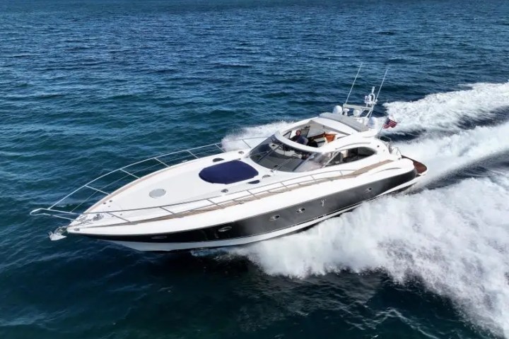 A sleek motor yacht cruising on the ocean with a city skyline in the background.