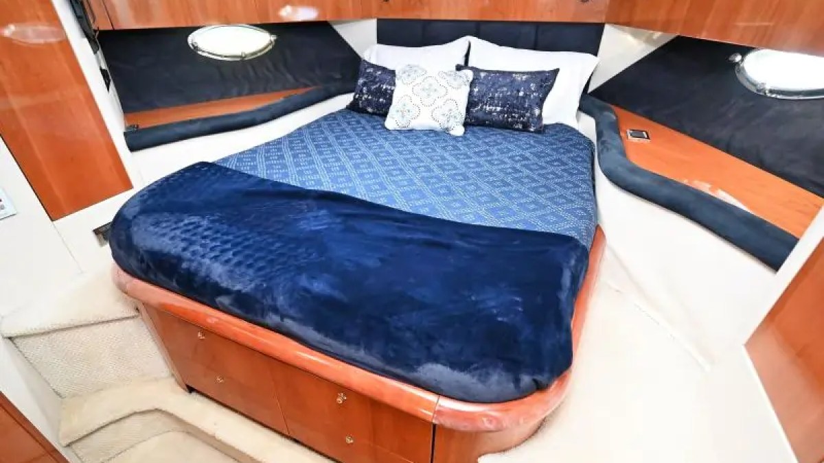 Cozy yacht cabin with a bed, blue bedding, and wooden cabinets.