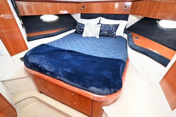 Cozy yacht cabin with a bed, blue bedding, and wooden cabinets.