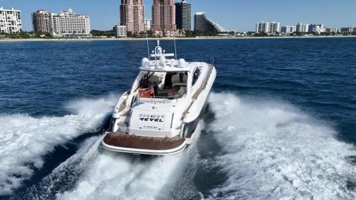 White yacht traveling in blue ocean near city skyline with tall buildings on a sunny day.