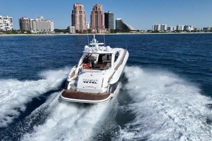 White yacht traveling in blue ocean near city skyline with tall buildings on a sunny day.