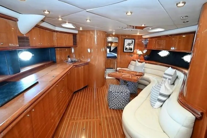 Luxurious yacht interior with wooden paneling, sofas, pillows, and ambient lighting.