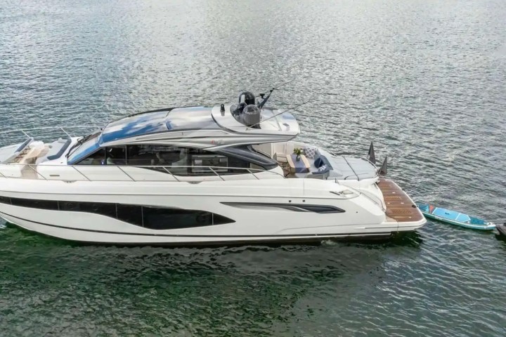 White yacht on water towing a blue paddleboard and black jet ski.