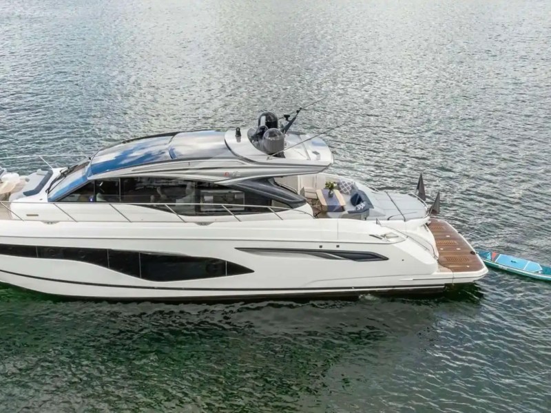 White yacht on water towing a blue paddleboard and black jet ski.