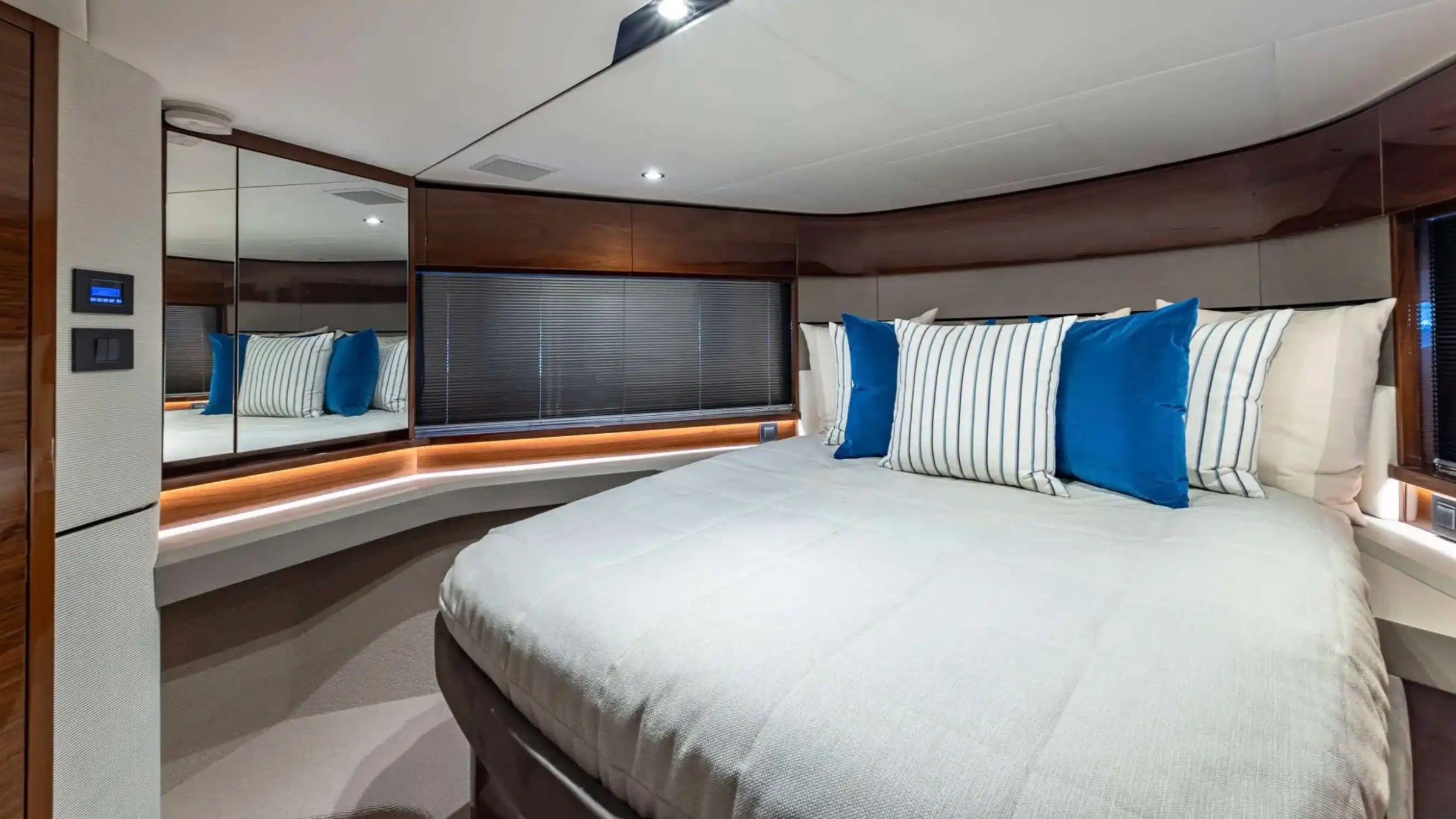 Modern bedroom with a large bed, blue and striped pillows, wood paneling, and mirrored wall.