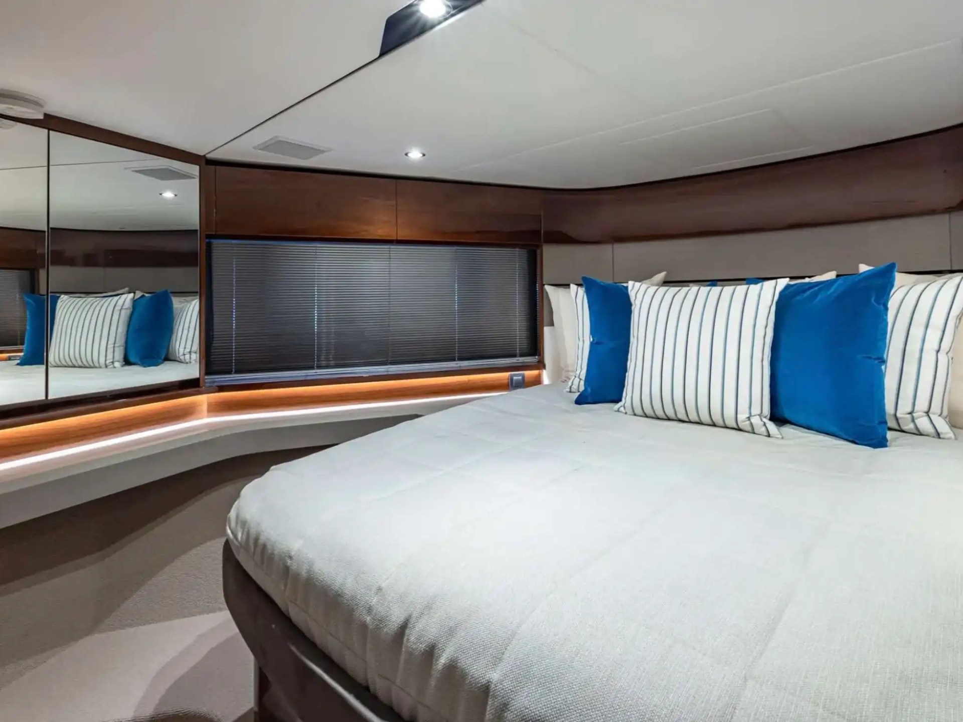 Modern bedroom with a large bed, blue and striped pillows, wood paneling, and mirrored wall.