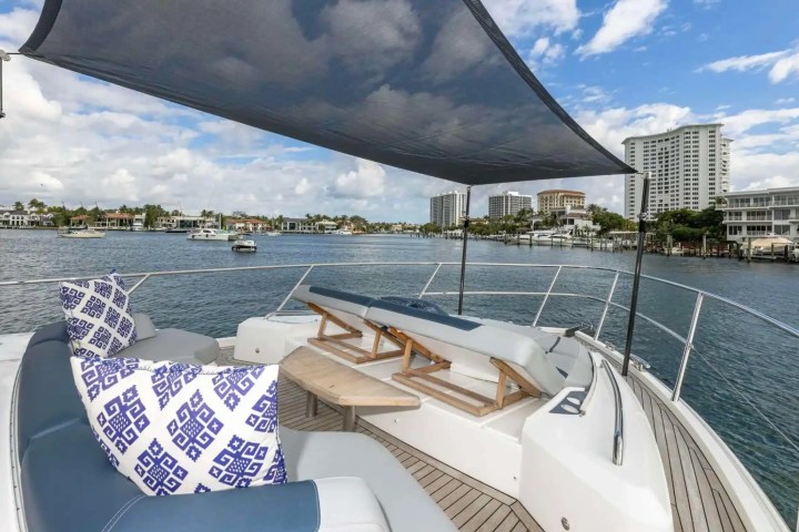 View from boat deck with sunshade, cushions, and waterfront buildings in the distance under a cloudy sky.