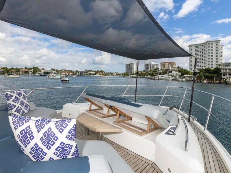 View from boat deck with sunshade, cushions, and waterfront buildings in the distance under a cloudy sky.