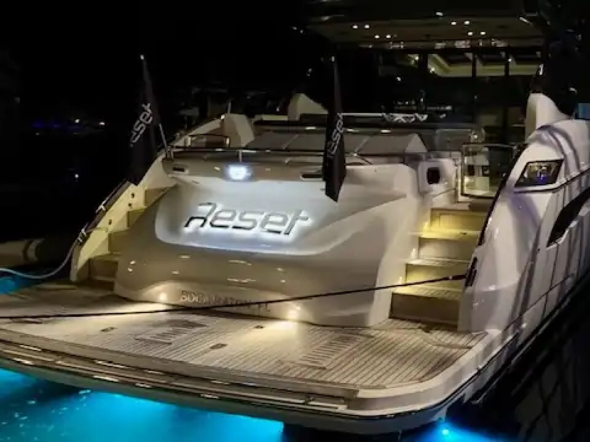 Luxury yacht named 'Reset' with illuminated steps and blue underwater lights at night.