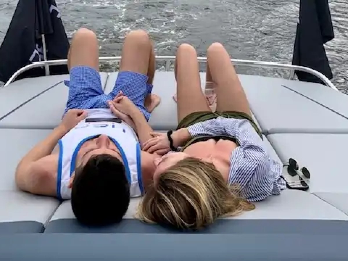 Two people relaxing on a boat deck, holding hands, with water visible behind them.