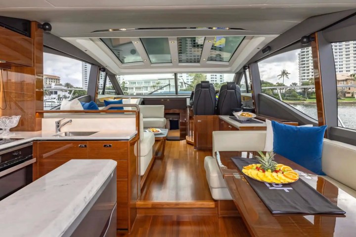 Luxurious yacht interior with wood floors, plush seating, and fruit platter on table. Large windows show a cityscape.