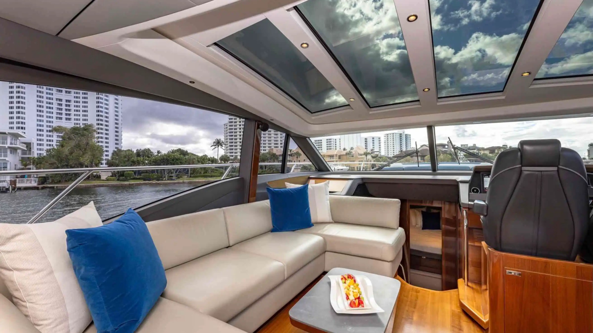 Luxurious yacht interior with leather seating, blue cushions, skylights, and cityscape view.