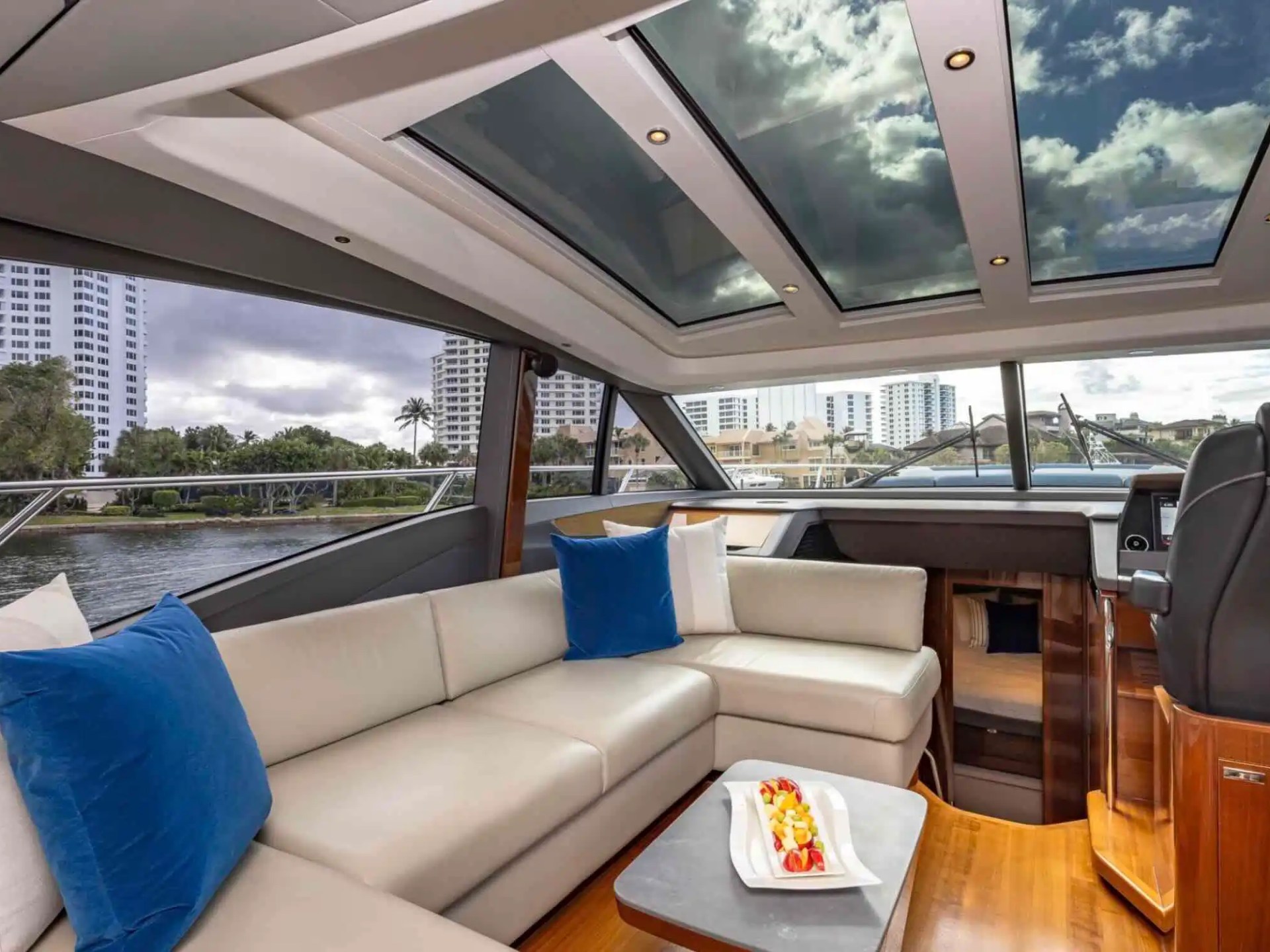 Luxurious yacht interior with leather seating, blue cushions, skylights, and cityscape view.