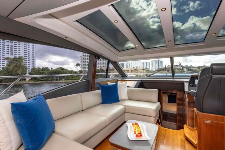Luxurious yacht interior with leather seating, blue cushions, skylights, and cityscape view.