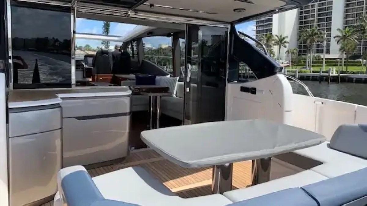 Outdoor seating area on a luxury yacht with table and cushioned benches, overlooking water and palm trees.