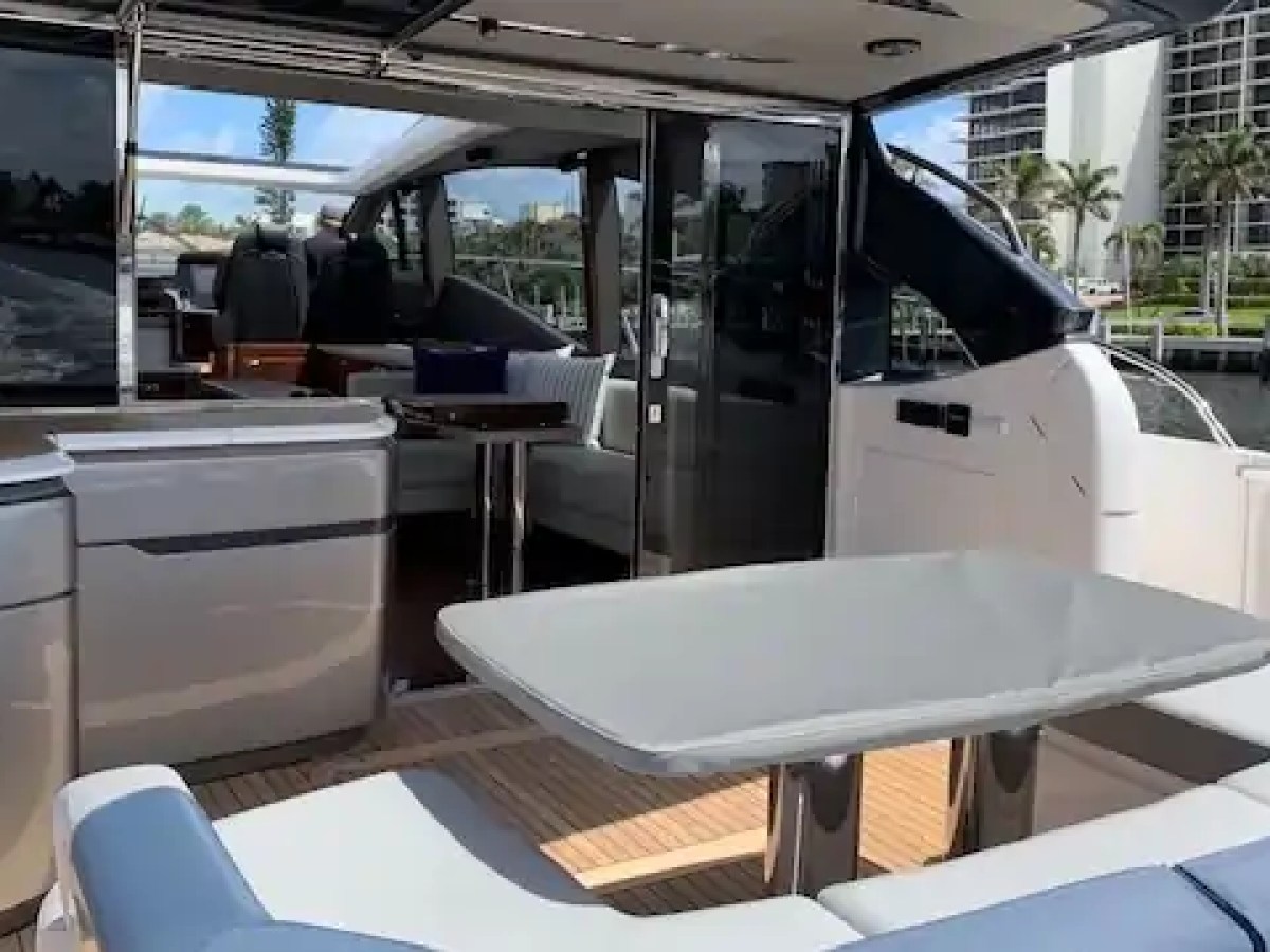 Outdoor seating area on a luxury yacht with table and cushioned benches, overlooking water and palm trees.