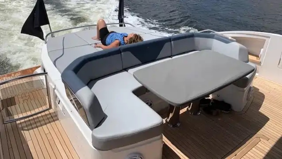 Person relaxing on yacht deck with cushioned seating and table, near water.