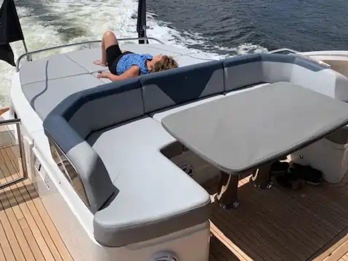 Person relaxing on yacht deck with cushioned seating and table, near water.