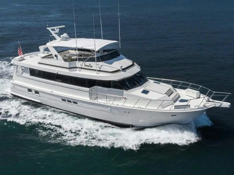 White yacht cruising on ocean waters, with an American flag at the rear.